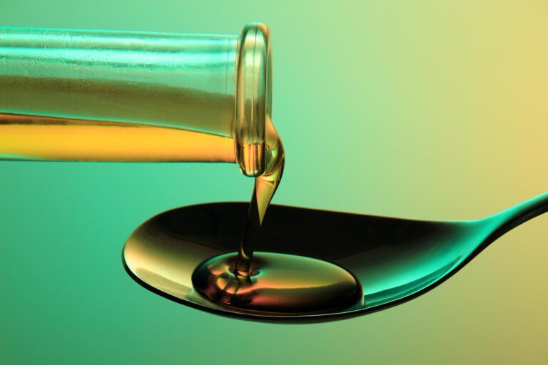 Oil pouring from a bottle into a spoon against a colorful background.