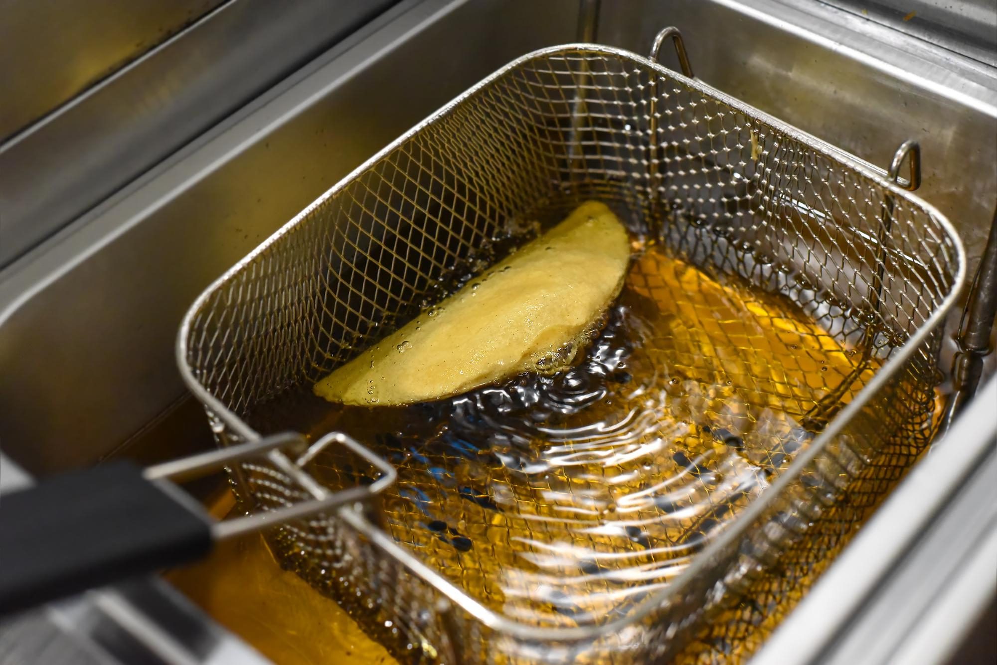 Golden fryer oil bubbles around a crispy snack in a mesh basket, showcasing efficient Fryer Oil Management Tips.