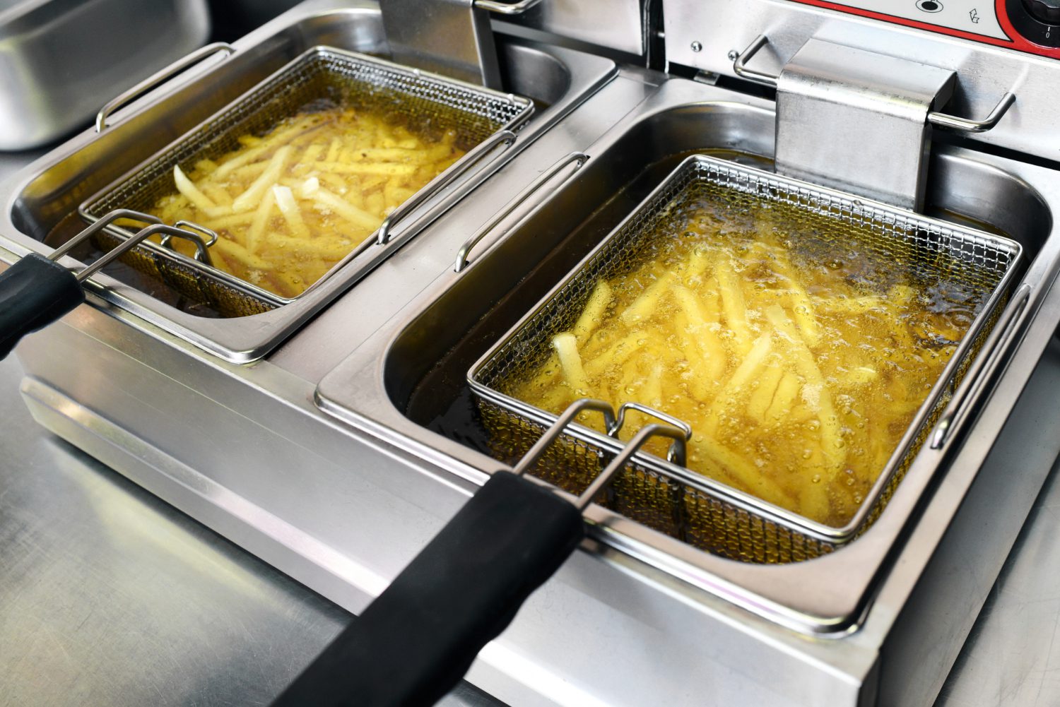 Two baskets of fries cooking in CanolaMAX oil in a commercial deep fryer.