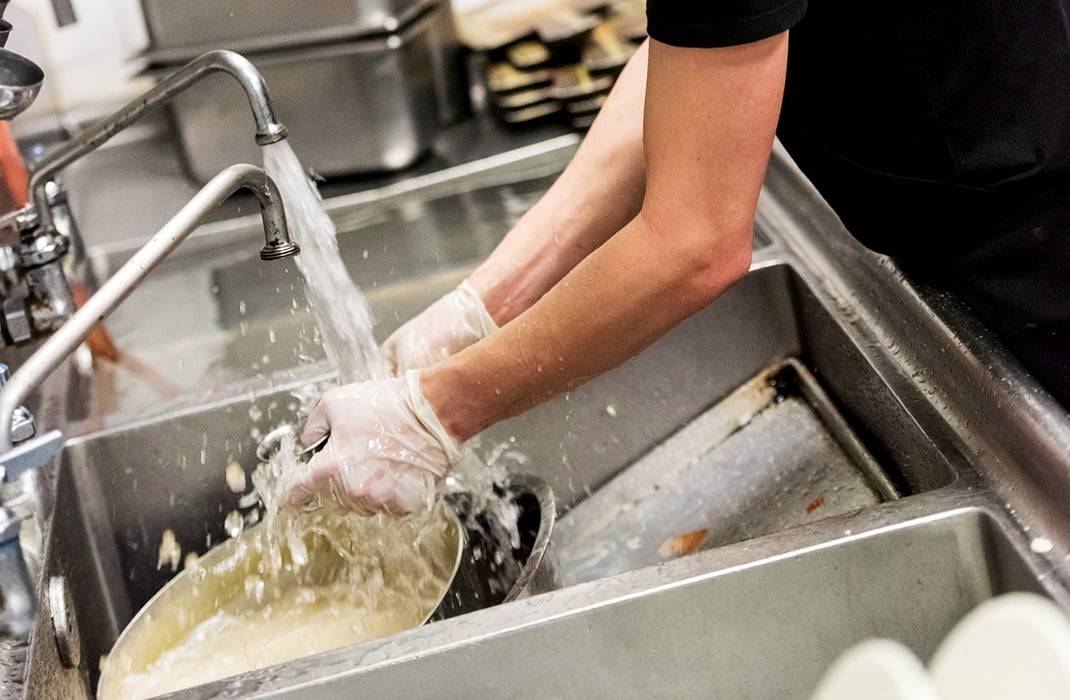 A person wearing gloves washing a pot in a sink, emphasizing the importance of thorough dishwashing during deep cleaning commercial kitchens.